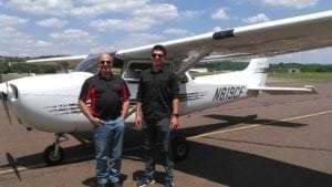 Two men outside an airplane smiling at the camera with glasses on